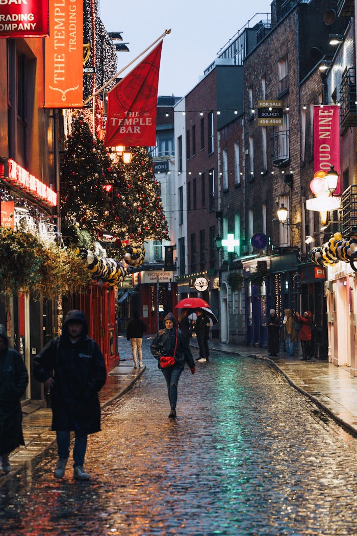 People walking in the rain at Temple Bar, Dublin with festive lights and umbrellas.