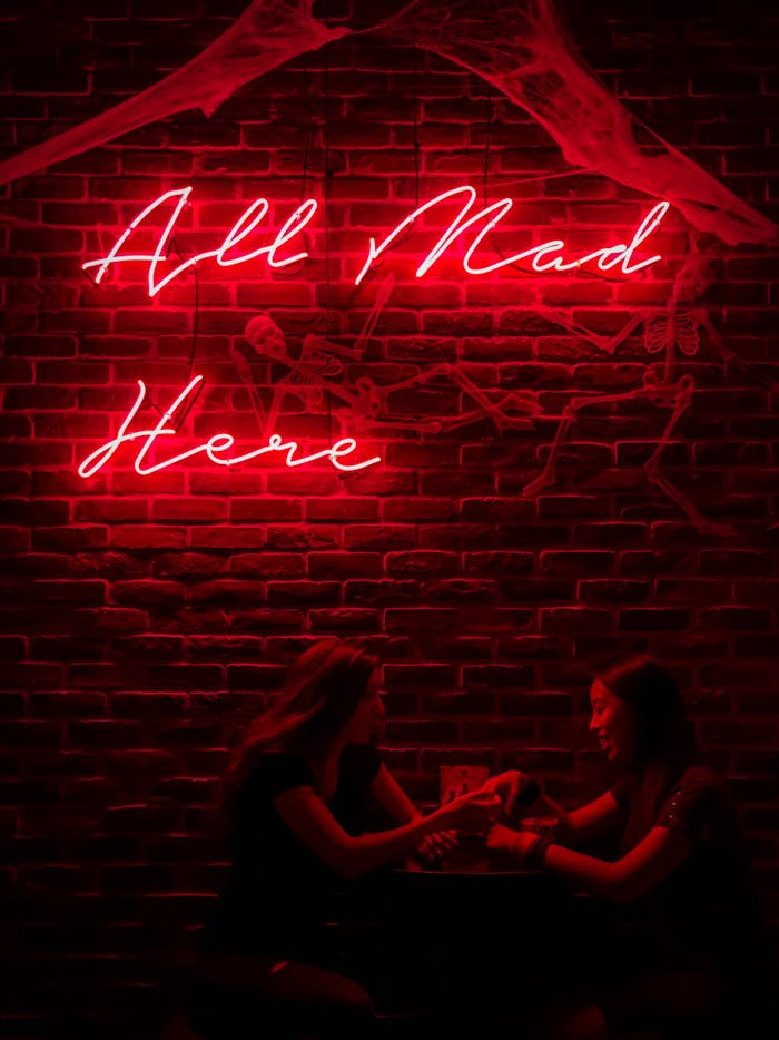 Two women enjoying a night out under a red neon sign with a playful phrase.