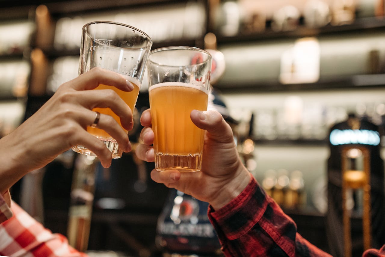 Close-up of friends toasting with beer glasses in a lively bar setting.